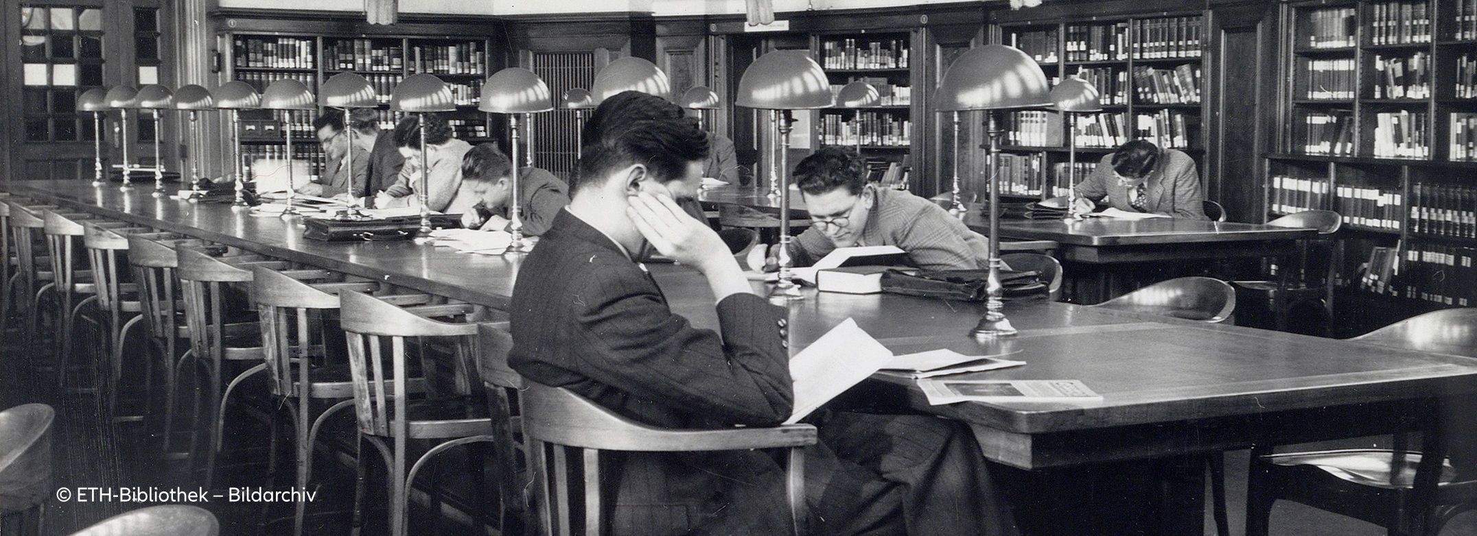 Schwarz-weißes Archivfoto von jungen Männern, die an einem langen Tisch in einer Bibliothek sitzen. Copyright: ETH Bibliothek Bildarchiv